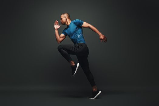 Full length portrait of a healthy muscular sportsman jumping isolated over dark background. Dynamic movement. Side view