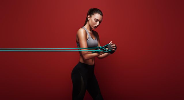 Sportswoman performs exercises for the muscles. Photo of young woman workout with resistance band isolated over red background. Strength and motivation.