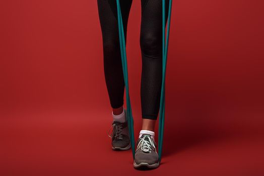 Close up of female legs in sportswear with expander exercising over red background