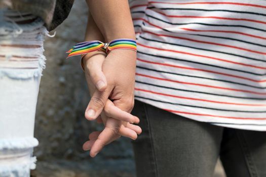 Close up of happy lesbian couple holding hands wearing rainbow flag wristband, LGBT love concept. High quality photo
