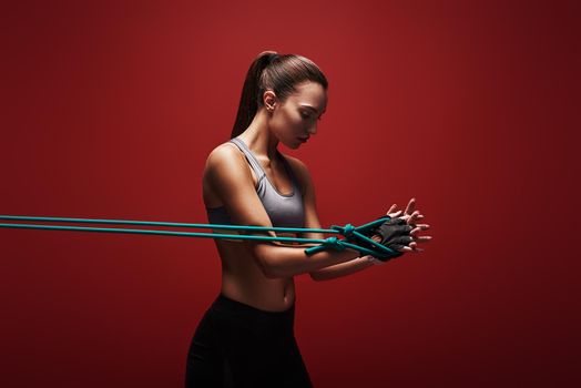 Sportswoman performs exercises for the muscles. Photo of young woman workout with resistance band isolated over red background. Strength and motivation.