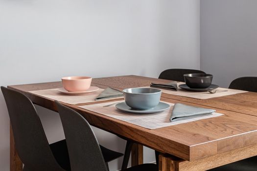 Stylish dining room interior with a wooden table set for three people with bowls and cutlery.