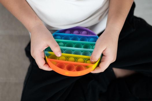 Faceless little boy playing pop it rainbow colors