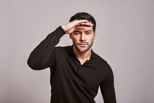 Closeup portrait of young serious curious squinting man, hand on head, peering ahead, searching for something, looking to the future at camera, isolated over white background. Sign, symbols