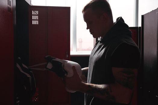 Close-up of focused muscular young boxer in sports clothing motivating himself before training while standing in gym locker room