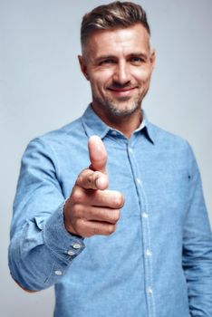 I am choosing you. Smiling handsome man pointing his finger and smiling at camera while standing against grey background. Positive emotion. Success