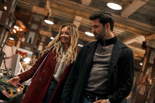 Stroll through the market together. Happy young joyful couple choosing handmade stuff and walking in rows at small street market. Autumn season, blond haired woman with her boyfriend are in street market