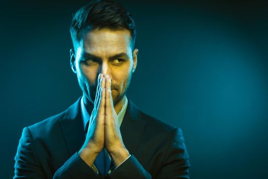 Serious Business Man Has an Idea How to Improve His Business. Strong White Man With Folded Hands in Creative Neon Light. Close-Up Portrait on Blue Background. High quality photo