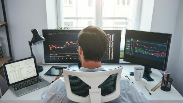 Trading stocks online. Back view of young businessman or trader working with graph and charts on computers at his modern office. Forex market. Trade concept. Investment concept