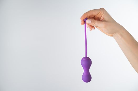 A faceless woman holding an electronic Kegel trainer for training pelvic floor muscles on a white background. Sex toy synchronized with a smartphone.