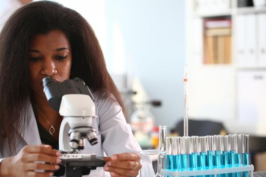 Black woman scientist student chemist in protective goggles are conducting research using microscope for bacterial contamination of water to search for vaccine to treat diseases in medicine.