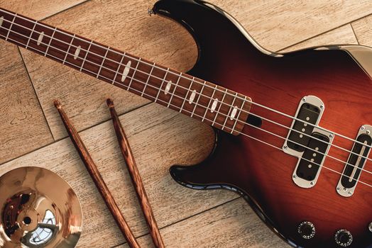 Top view of electronic guitar with wooden sticks and golden cymbal lying on wooden background. Musical instruments. Music equipment