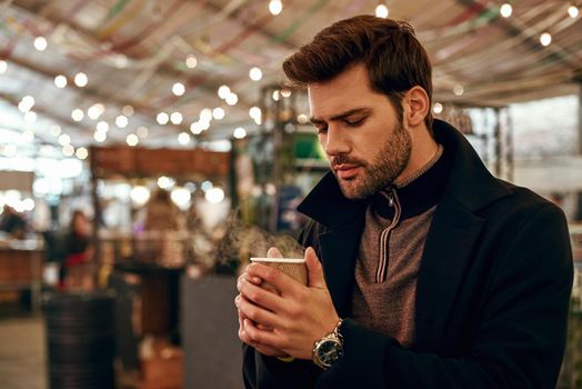 Hot sweet mulled wine. Close-up of man drinking mulled wine at the street fair market. Cold season. Close-up photo of brunette stylish man