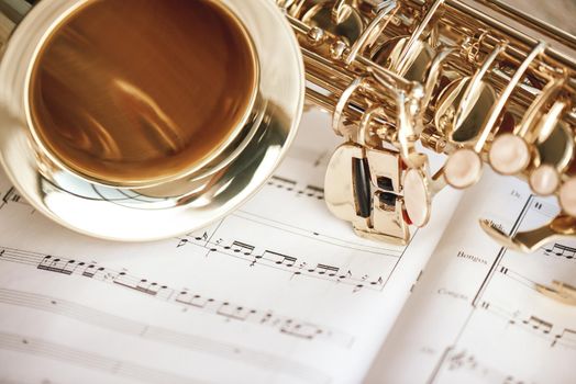 Romantic morning. Close up view of saxophone and cup of coffee lying on the musical notes. Musical instruments.