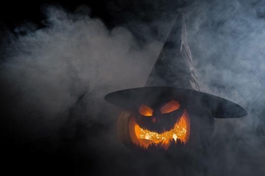 A creepy pumpkin with a carved grimace in the smoke. Jack o lantern in the dark