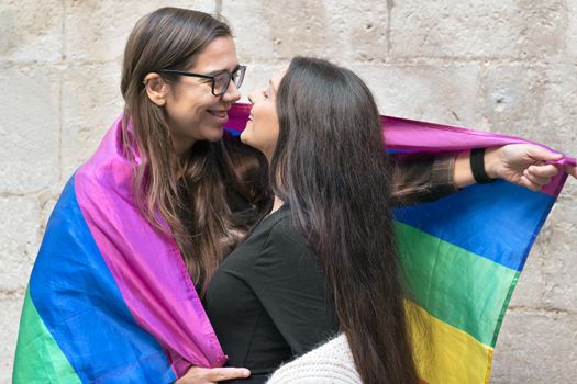 Portrait of an affectionate young lesbian couple hugging each other while standing together in front of a stone wall outside. High quality photo.