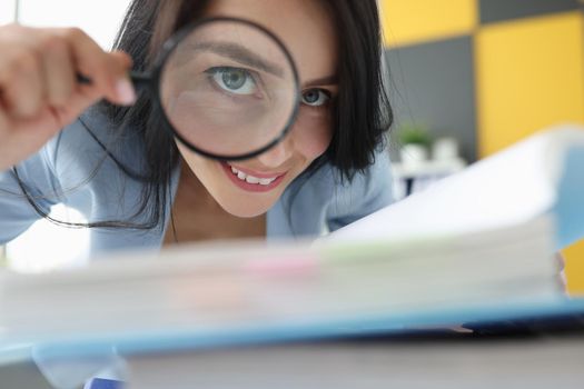 Joyful woman looks through a magnifying glass, close-up. Financial audit, detective agency, investigation, document archiving