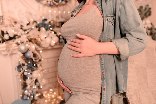 Close up of happy smiling pregnant woman touching her belly over a christmas tree background