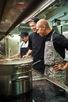 Great job. Cheerful professional chef looking how his two assistants are cooking in a restaurant kitchen. Preparing food