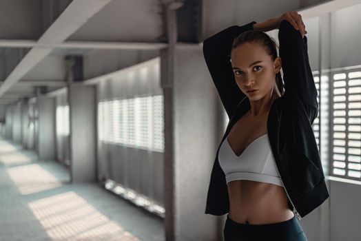 Young woman in sportive clothes is doing warming up exercises near the stadium. Hands stretching