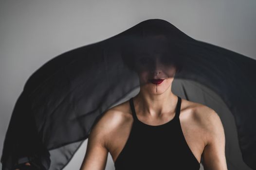 Redhead woman with a black veil on her head in a dark studio. A girl with an earring in her nose smiles slyly. Witch Makeup. Halloween costume