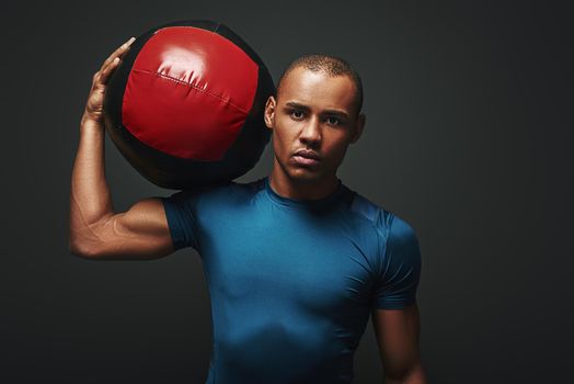 Close up portrait of a crossfit male athlete working out with exercise ball. Handsome muscular athletic sportsman standing with the ball over dark background in studio. Endurance concept