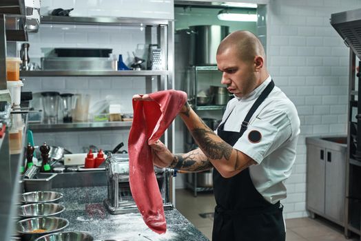 Italian food. Handsome professional chef holding a dough for homemade pasta while standing in restaurant kitchen. Cooking process