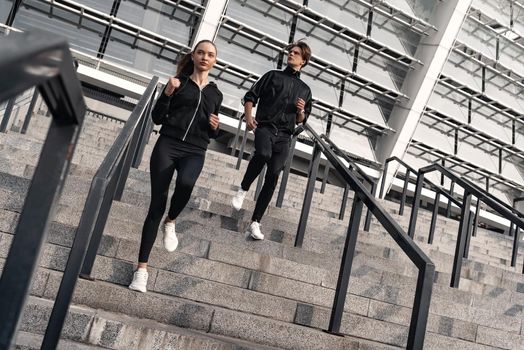 Early morning workout. Young couple running downstairs near the football stadium. Living healthy lifestyle.