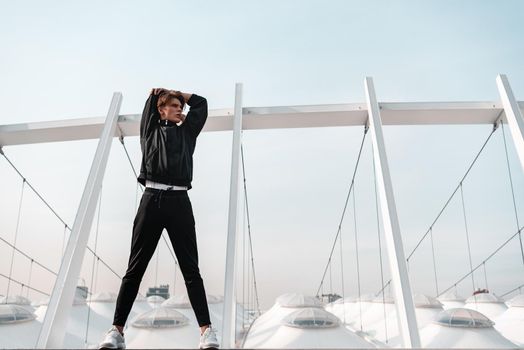 Young man in sportive clothes is doing warming up exercises near the stadium. Hands stretching