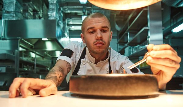 Ready to eat Portrait of handsome young chef decorating delicious chocolate cake under lamp light on a kitchen table. Sweets