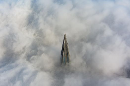 Russia, St. Petersburg, 14 October 2021: The top of the tallest skyscraper in Europe above the clouds, the building of the Gazprom oil company, the spire of a metal and glass structure. High quality photo