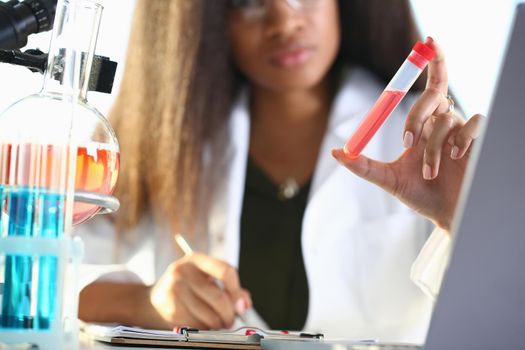 A female chemist holds test tube of glass in his hand overflows liquid solution potassium permanganate conducts an analysis reaction takes various versions reagents using chemical manufacturing.