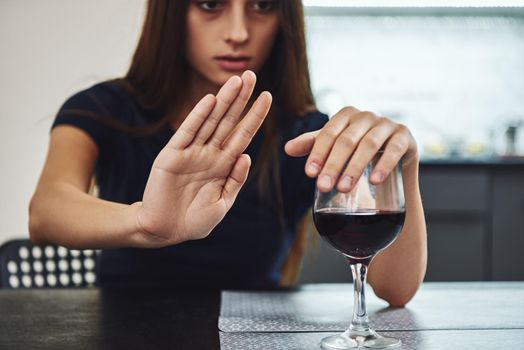 A glass of red wine standing on the table with female hands on it. Woman refuses to drink alcohol. Female alcoholism concept.