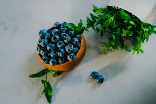 A small wooden bowl with berries. Juicy and ripe blueberries in an eco-friendly dish. Sprigs of fresh mint in a kraft bag. The concept of healthy eating and nutrition