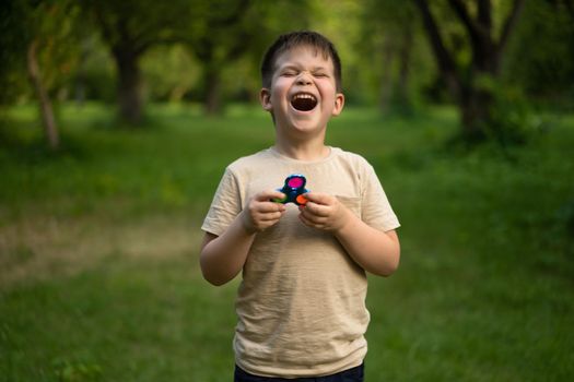 Funny Boy Laughing in the Sunny Field in the Park. Child Takes Colorful Spinner for a Walk. Forest Background. High quality photo