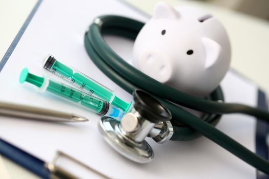 Syringe stethoscope and piggy bank for money on medicine doctor desk health insurance working ability concept