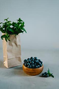 A small wooden bowl with berries. Juicy and ripe blueberries in an eco-friendly dish. Sprigs of fresh mint in a kraft bag. The concept of healthy eating and nutrition