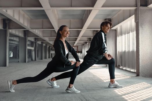 Young man and woman in sportive clothes are doing warming up exercises at parking near the stadium. Hands and legs stretching