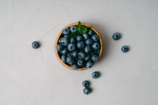 A small wooden bowl with berries on a gray background. Juicy and ripe blueberries in an eco-friendly dish. Top view of a bowl of blueberries. Berries on a gray textured background.