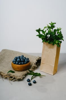 Eco package with fresh mint and wooden bowl with blueberries. Delicious and juicy berries in dishes made of natural material.