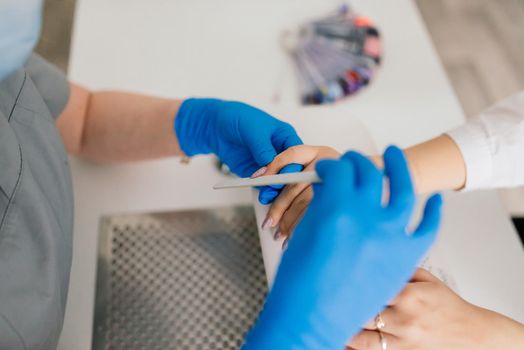 Smiling woman at beauty salon has a manicure from manicure master. Master is using nail file.