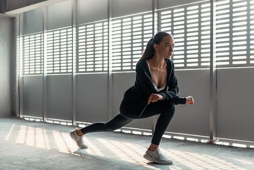 Young woman in sportive clothes is doing warming up exercises near the stadium. Legs stretching