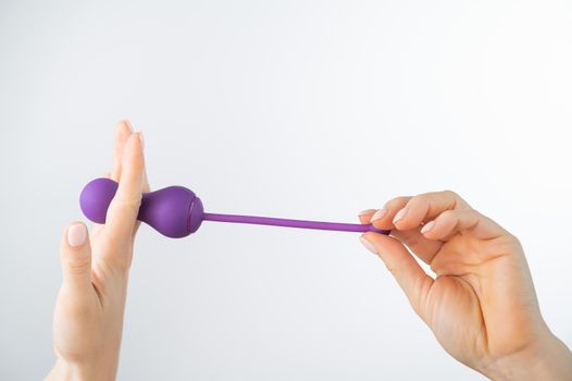 A faceless woman holding an electronic Kegel trainer for training pelvic floor muscles on a white background. Sex toy synchronized with a smartphone.