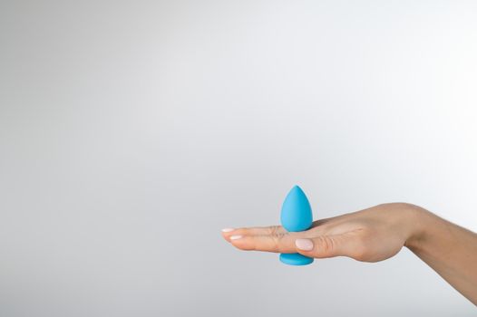 Woman holding a blue anal plug on a white background. Adult toy for alternative sex.