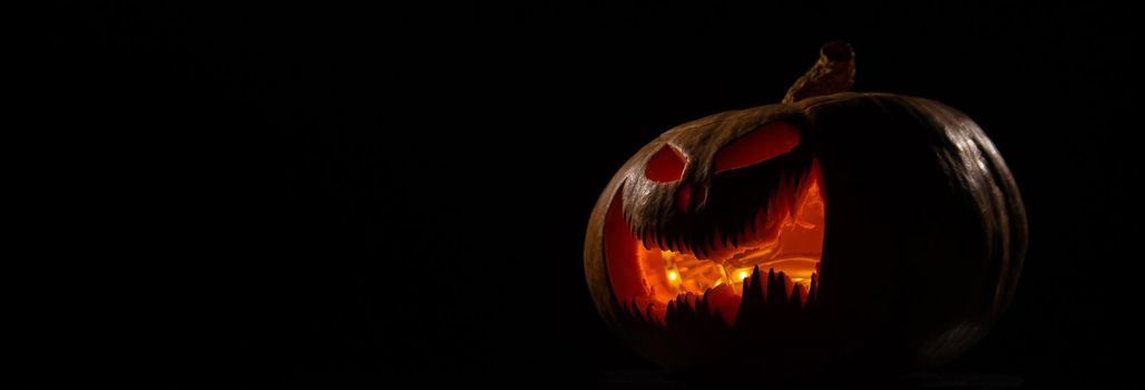 A creepy pumpkin with a carved grimace glows. Jack on a lantern in the dark