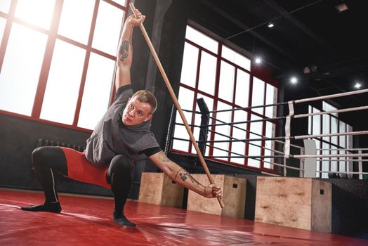 Focused young muscular athlete in colored sports clothing warming up his muscles before training in black boxing gym