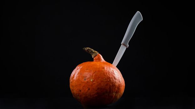 Knife in a pumpkin on a black background. Halloween symbol. Isolate