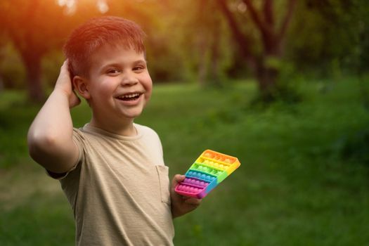 White Little Boy Enjoys Popping Bubbles on His Pop It in the Yard. A Little One Waiting for his Friends to Play Pop It in the Yard. Natural Background. High quality photo