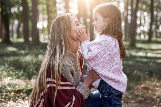 Little girl and her mother in the forest. Woman is wearing a stylish hat and knitted coat, girl is in pink bright sweater