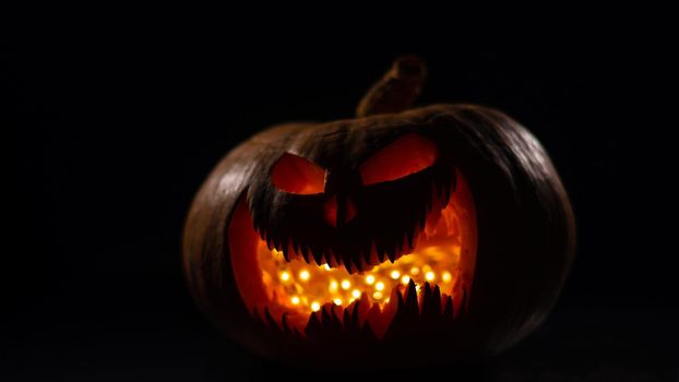 A creepy pumpkin with a carved grimace glows. Jack on a lantern in the dark